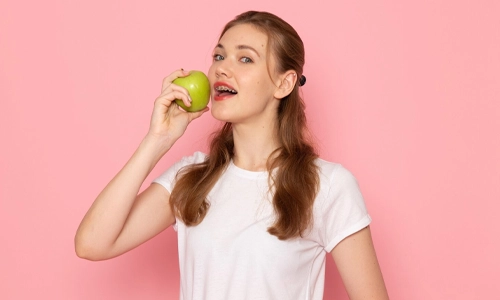 woman-eating-green-apple-pink-background