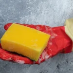 a hand holding kitchen sponge while wearing protective gloves.