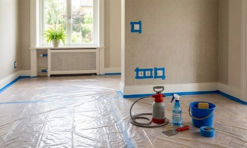 Room prepared for wallpaper removal with plastic drop cloths and taped baseboards.