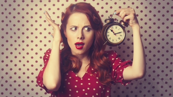Portrait of a surprised redhead girl with alarm clock on Polka dot background.