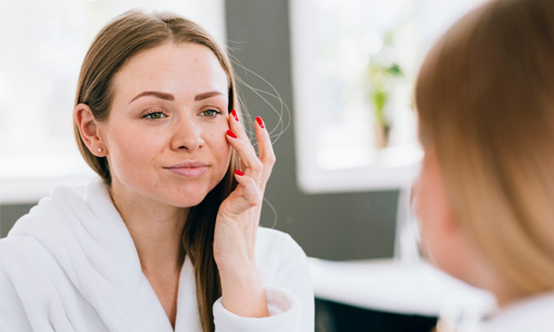 A woman applying cream on her face in front of a mirror