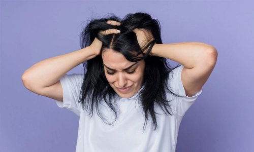Disappointed young brunette caucasian girl holds head and looks down isolated on purple wall