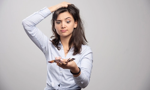 Confused woman holding makeup brushes and scratching her head.