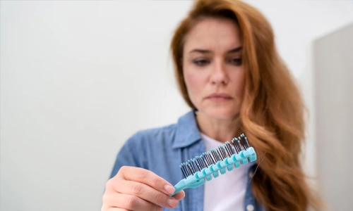 Concerned woman looking at hair loss on her brush.