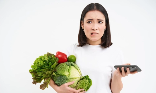 Portrait of young woman holding vegetables organic food holds smartphone with concerned worried face.