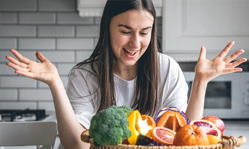 Image of a young woman and a basket of fruits and vegetables in the kitchen