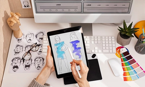 Person sketching fashion designs on a tablet beside a computer and color swatches