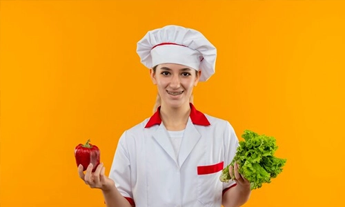 Chef holding a red bell pepper and fresh lettuce against an orange background
