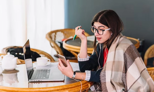 Woman using a laptop and smartphone while working remotely at a café