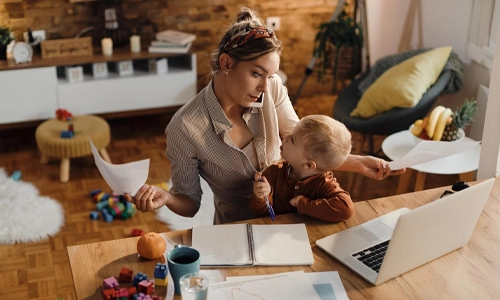 Mother working from home with her toddler while reviewing papers at a laptop