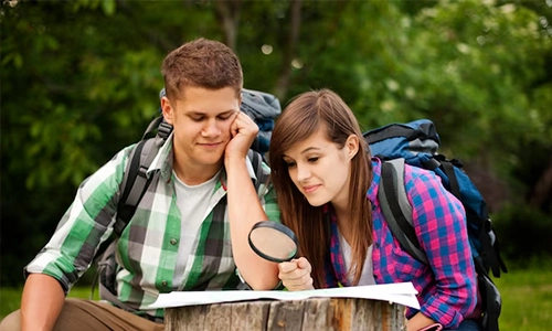 Two young male and female hikers studying a map with a magnifying glass during an outdoor trip