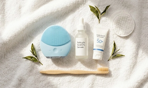 Salicylic acid serum, sunscreen, facial cleansing brush, toothbrush, and cotton pads arranged on a white towel.